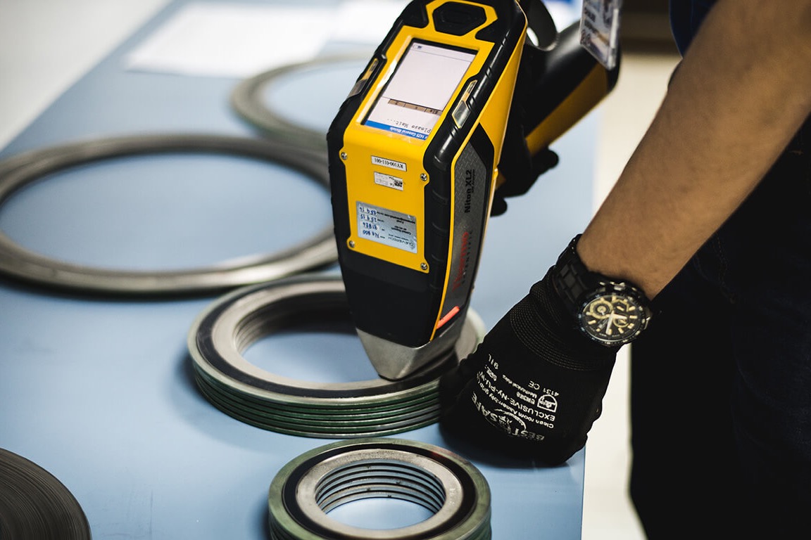 A handheld XRF analyser held against a stack of bearing rings on a bench.